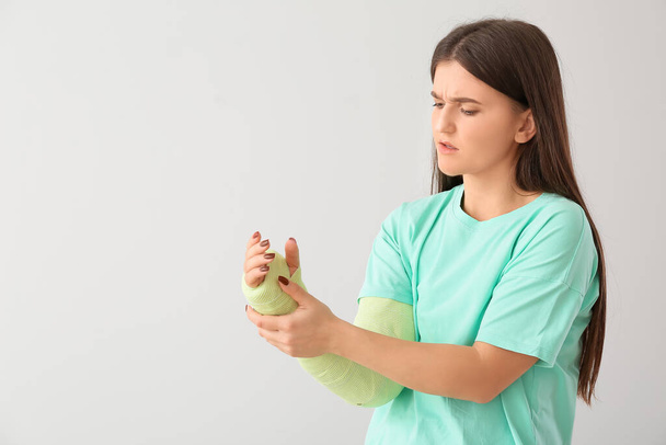 Junge Frau mit gebrochenem Arm auf hellem Hintergrund - Foto, Bild
