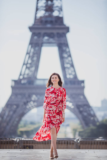 Женщина с черными волосами в красном платье стоит на фоне Эйфелевой башни в Париже - Фото, изображение