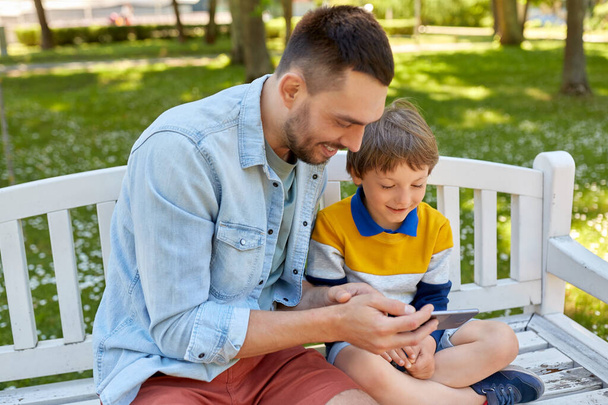 father and son with smartphone at park - Photo, Image