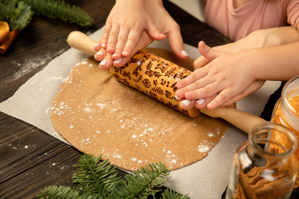 Κοντινό πλάνο παιδί και γυναικεία χέρια κάνοντας εορταστικά μπισκότα με πλάστη. - Φωτογραφία, εικόνα