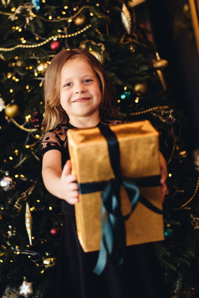 Little girl with gift near christmas tree. Happy child waiting for the holiday - Фото, зображення
