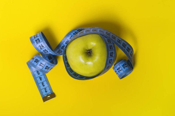 gelber Apfel mit blauem Maßband auf gelbem Hintergrund Diät und Sportkonzept von oben. - Foto, Bild