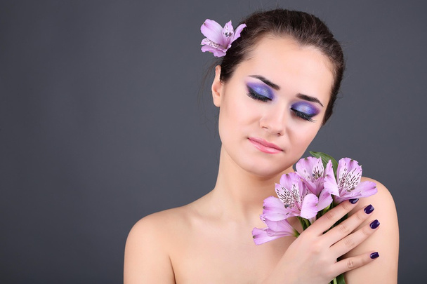 όμορφη νεαρή γυναίκα με λουλούδια σε γκρι φόντο - Φωτογραφία, εικόνα
