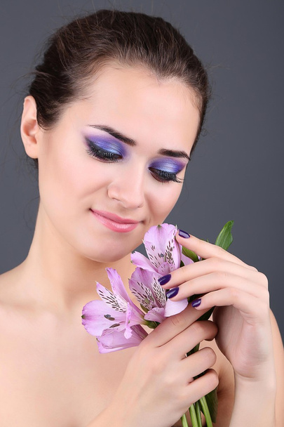 Beautiful young woman with flowers on gray background - Zdjęcie, obraz