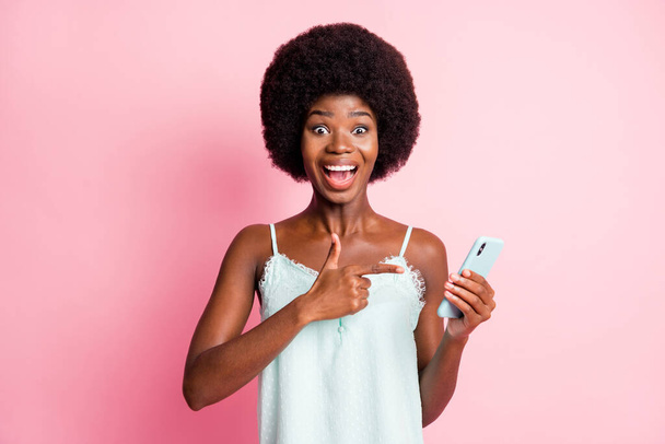 Portret van mooie bruin haar stijlvolle trendy vrouw dragen singlet punt houden promotie smartphone geïsoleerd op roze kleur achtergrond - Foto, afbeelding