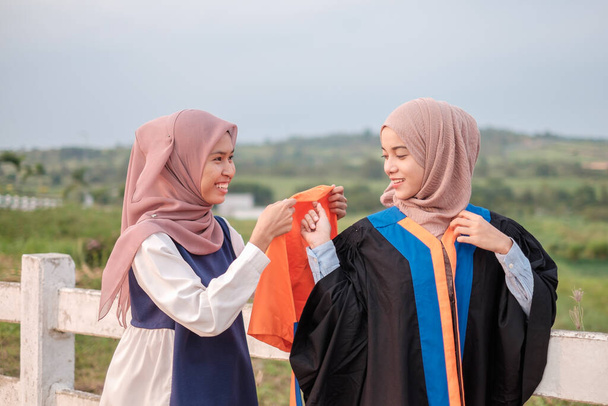 Όμορφες Ασιάτισσες Μουσουλμάνες φοιτήτριες που ταιριάζουν με το φόρεμα αποφοίτησης και ποζάρουν ευτυχισμένες πριν την τελετή αποφοίτησης. - Φωτογραφία, εικόνα