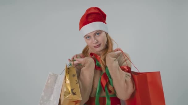 Happy girl in Santa hat, smiling holds gift sale bags isolated on a white grey. - Materiał filmowy, wideo