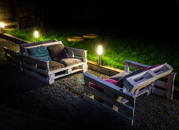 Jardim noturno com sofá auto-feito de paletes é iluminado lâmpadas de jardim - Foto, Imagem