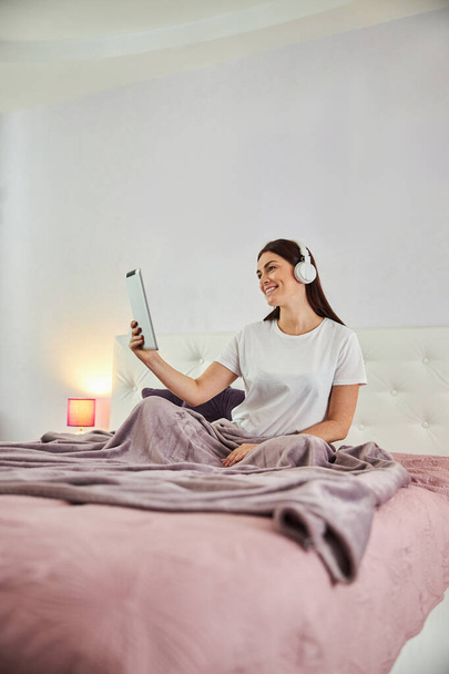Ama de casa usando una tableta para comunicarse desde su dormitorio - Foto, Imagen