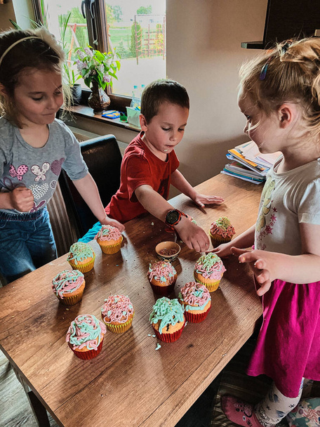 カップケーキを焼く子供たちのグループ,材料を準備,トッピング,クッキーを飾るためのスプリンクル.家庭のキッチンで一緒に働いている子供たちの料理。幸せな家庭の概念 - 写真・画像