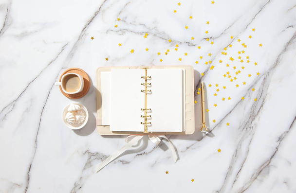 Notebook with empty pages for your text, pen, coffee cup, milk, small gift boxes with pink ribbon and golden sparkles on white marble table. New Year and Christmas concept, top view. Festive holidays - Foto, Imagen