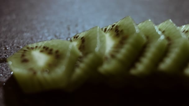 Sappige verse kiwi fruitschijfjes op een zwart marmeren snijplank. Macro uitzicht. Langzame beweging - Video