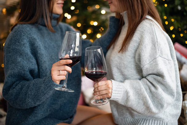 The girls are holding glasses with red wine in their hand. Celebrating new year and christmas.Christmas home decoration - Photo, Image
