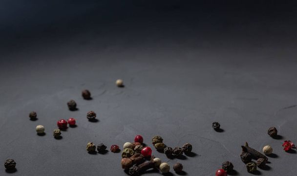 Mélange de poivre et clous de girofle. Des grains de poivre noirs, rouges et blancs isolés sur fond de pierre noire. Gros plan, espace de copie - Photo, image