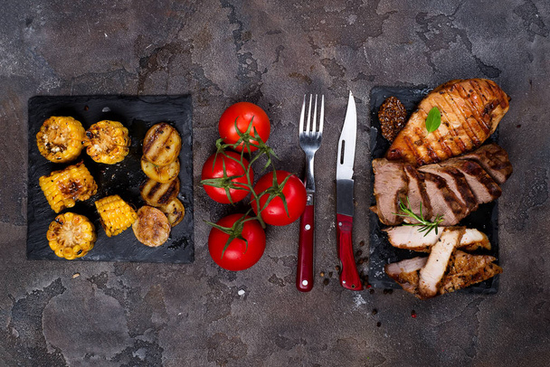 Fresh three types of grilled steak (chicken, pork, beef) on slate plate with herbs, tomato, corn and grilled potatoes on stone background with copy space, flat lay - 写真・画像