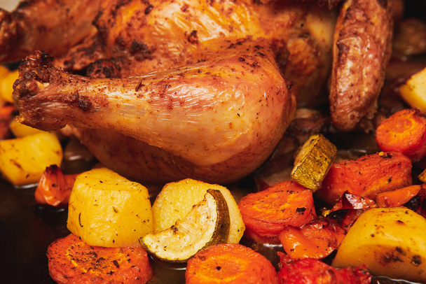 Egész sült csirke vagy pulyka különböző zöldségekkel a fekete tálcán. Friss csirke, arany ropogós kéreggel. Karácsonyi ünnepi recept curryvel. Lábközeli kép. - Fotó, kép