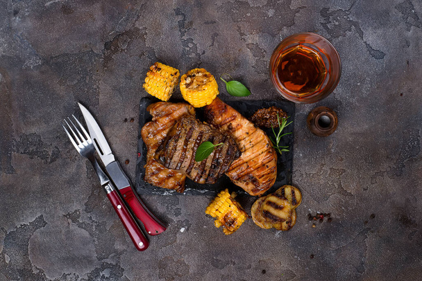 Fresh three types of grilled steak (chicken, pork, beef) on slate plate with herbs, juice and grilled potatoes on stone background with copy space, flat lay - Φωτογραφία, εικόνα