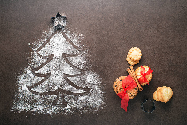 Christmas tree made from flour on a dark table, kitchen utensils and cookies. holiday, celebration and cooking concept. new year and christmas postcard - Foto, Imagem
