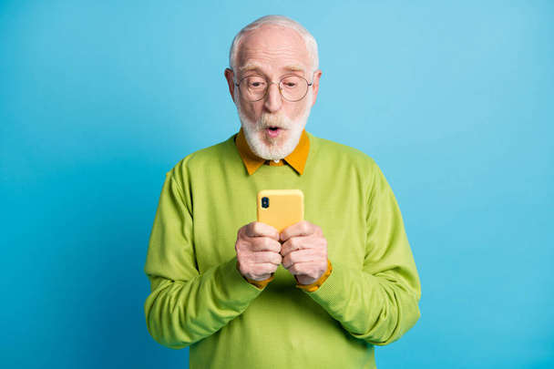 Photo of pensioner grandpa open mouth excited hold smartphone wear specs green sweater isolated blue color background - Foto, imagen