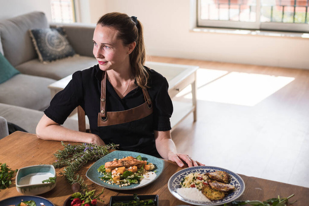 Jeune blogueur alimentaire suédois attrayant posant devant une table pleine de plats alimentaires. Jeune fille assise devant une table en bois mangeant de la nourriture végétarienne et des plats sains. Style de vie végétarien - Photo, image