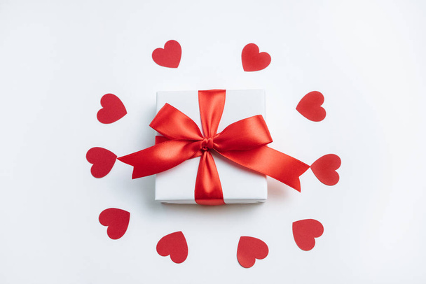 Geschenkdoos met rood lint en hartjes op witte achtergrond. Valentijnskaart. Bovenaanzicht, vlak lay. - Foto, afbeelding