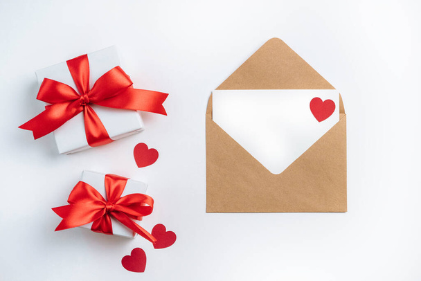 Cajas de regalo con cinta roja y sobre marrón con tarjeta en blanco sobre fondo blanco. Banner de San Valentín con espacio libre. Vista superior, plano. - Foto, Imagen