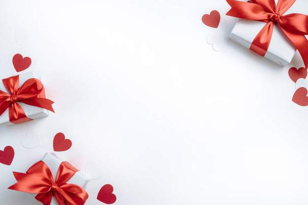 Подарункові коробки з червоною стрічкою та сердечками на білому тлі. День Святого Валентина банер з вільним простором. Вид зверху, плоский ліжко
. - Фото, зображення
