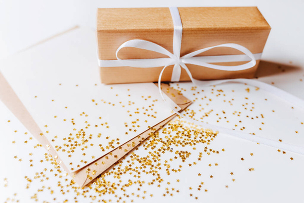 Gift and blank note with envelope, gold glitter stars on white background - Φωτογραφία, εικόνα