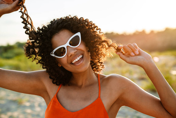 Image of amazing pretty smiling young african woman walking at the beach outside in sunglasses - Photo, Image