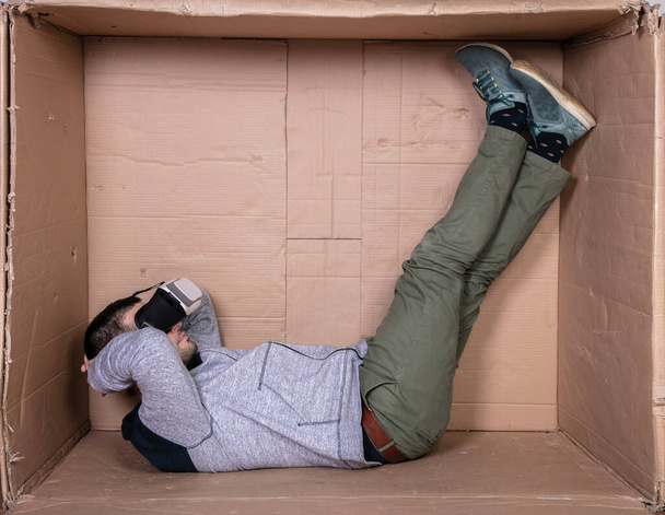 man with glasses for virtual reality, sitting in a cardboard room and entertained - Fotografie, Obrázek