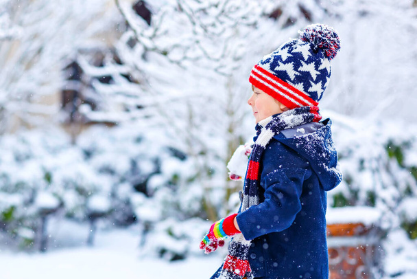 Zabawny chłopiec w kolorowych ubraniach bawiący się na zewnątrz podczas silnych opadów śniegu - Zdjęcie, obraz