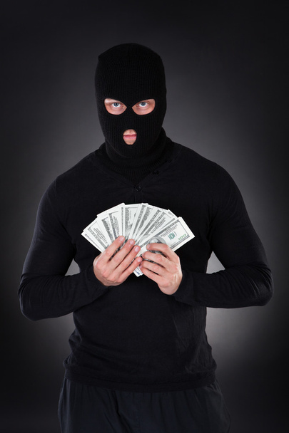 Criminal in a balaclava holding a fistful of money - Фото, зображення