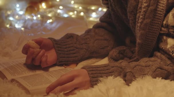 Σκοποβολή της ανάγνωσης νεαρή γυναίκα σε πλεκτό πουλόβερ τρώει μανταρίνι - Πλάνα, βίντεο