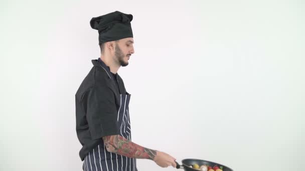 Boční pohled profesionálního kuchaře házet zeleninu ve wok proti bílému pozadí - Záběry, video