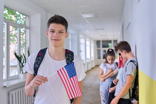 Male student teenager with USA flag inside college, group of students background - Foto, afbeelding