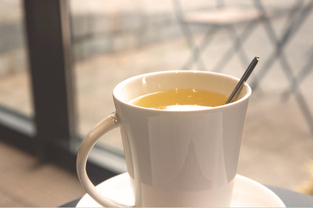 Taza de cerámica blanca con té de jengibre caliente en una mesa en un café. Bebida caliente. Café de la mañana afuera - Foto, Imagen