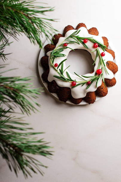 Christmas Bundt cake with white glaze and spruce branches over light background. Top view.  - Photo, Image