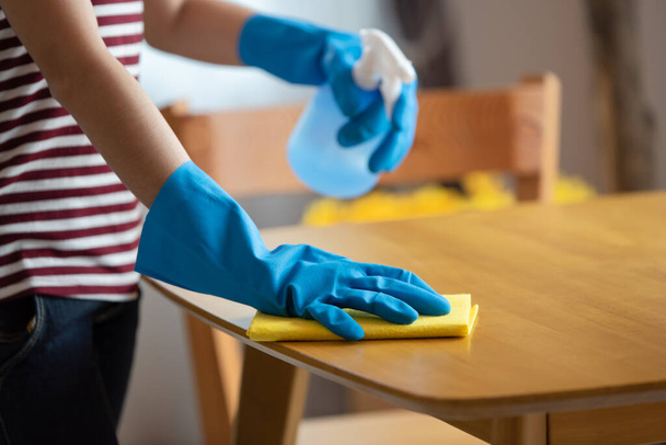 Close up de mulheres dona de casa mãos em luvas de borracha segurando spray limpando a mesa na sala de estar em casa, conceito de limpeza feliz - Foto, Imagem