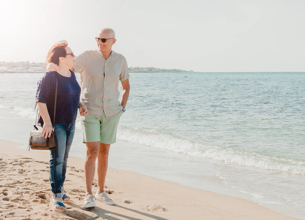 Ehepaar mittleren Alters spaziert am Meer entlang - Rentner genießen ihre Freizeit beim Spazierengehen in der Natur - warmer Filter im Hintergrund - Foto, Bild