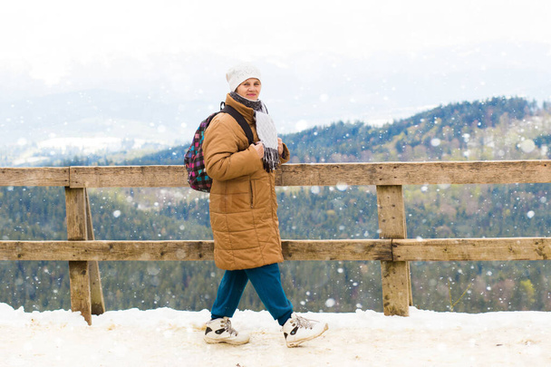 Glückliche Touristin mit Rucksack steht auf Aussichtsplattform und blickt auf schöne schneebedeckte Berge im Winter - Foto, Bild