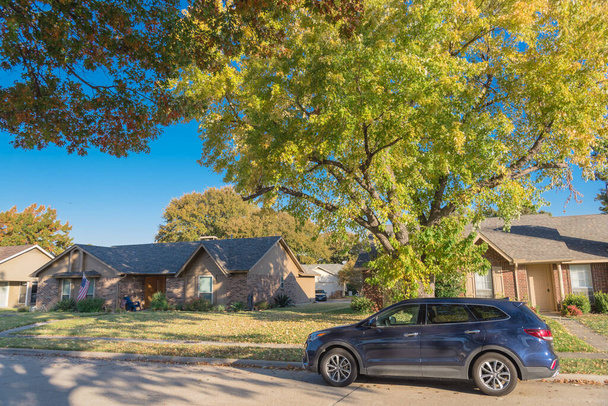 ダラス,テキサス州,アメリカの典型的なバンガローの家の前庭でカラフルな紅葉の木の下の住宅街の駐車車 - 写真・画像