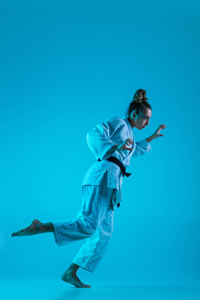 Genç profesyonel judocu kız mavi stüdyo arka planında neon ışıkta izole edilmiş. Sağlıklı yaşam tarzı, spor anlayışı. - Fotoğraf, Görsel