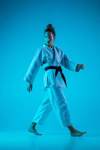 Profesyonel kadın judocu, mavi stüdyo arka planında neon ışıkta izole edilmiş şekilde poz veriyor. Sağlıklı yaşam tarzı, spor anlayışı. - Fotoğraf, Görsel