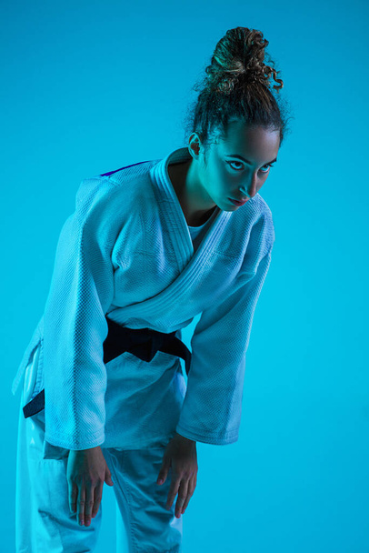 Professional female judoist training isolated on blue studio background in neon light. Healthy lifestyle, sport concept. - Photo, Image