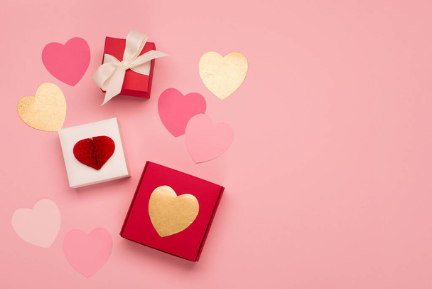 パステルピンクの背景にピンクの紙の心と赤いギフトボックス。バレンタインデーのコンセプト。フラットレイアウト、トップビュー、コピースペース。バレンタイン、誕生日、女性や母の日のための祭りの休日の挨拶カード. - 写真・画像