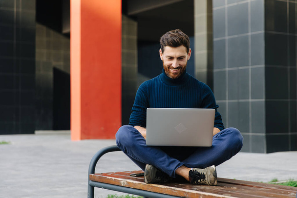 Glimlachende man met laptop voor werk buitenshuis - Foto, afbeelding