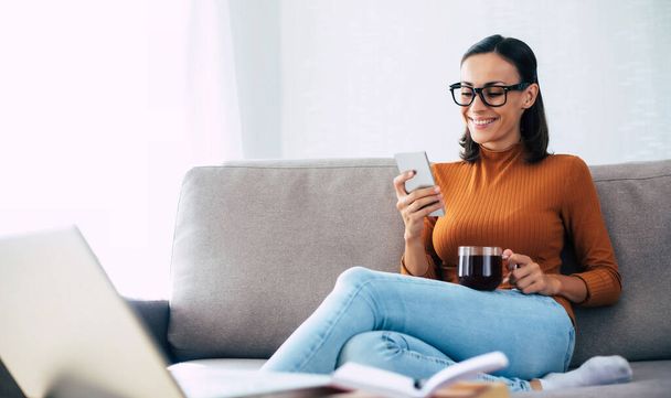 Happy excited beautiful woman with smart phone on the couch - Foto, Bild