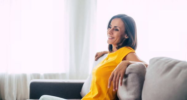 Beautiful calm confident brunette woman is resting on the couch at home during holidays - Valokuva, kuva