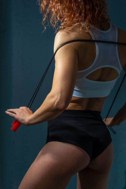 atleet meisje met vlekkeloze spieren en atletisch lichaam, met een springtouw, poseren tegen een getextureerde blauwe muur achtergrond Mooie sport meisje doen oefeningen met springtouw. - Foto, afbeelding