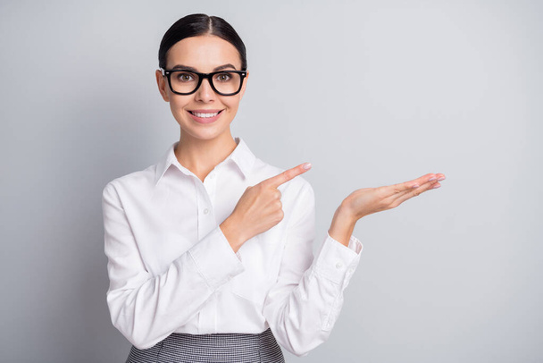 Photo of young business woman direct finger hold palm empty space wear specs white shirt isolated grey color background - Φωτογραφία, εικόνα